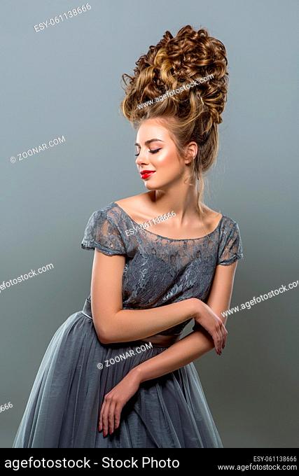 beautiful young woman in grey long dress with big curly hairstyle. studio beauty shot on grey background. copy space