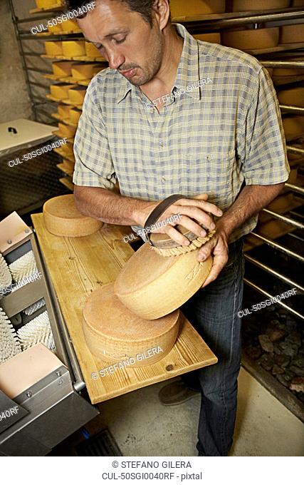 Worker finishing wheel of cheese in shop