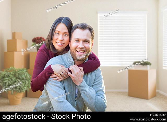 mixed-race caucasian and chinese couple inside empty room with moving boxes