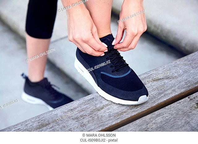 Close up of woman with foot raised on bench tying shoelace
