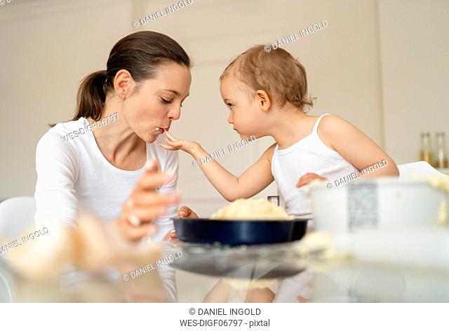 Little girl feeding mother while making a cake in kitchen at home