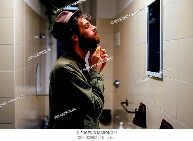 Bearded young man brushing beard in bathroom