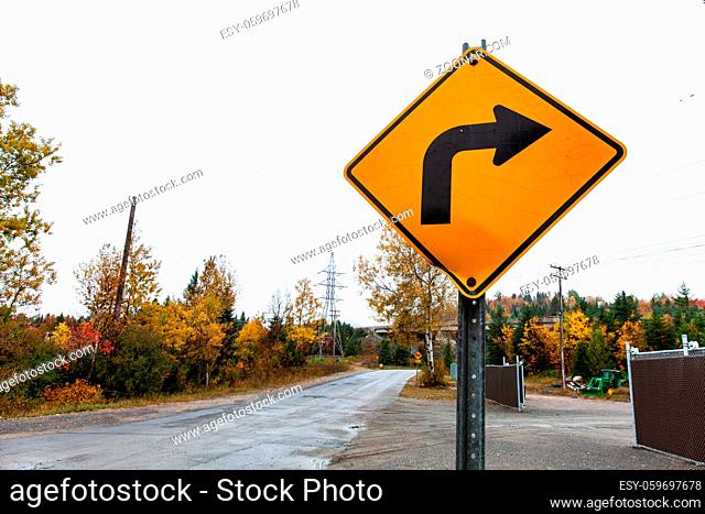 Picture taken in Quebec, Canada, while autumn colors were very present. Perspective from the side of the road with a turning right sign