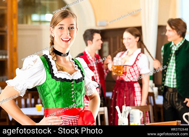 Young people in traditional Bavarian Tracht in restaurant or pub, one woman is standing in front, the group in the background