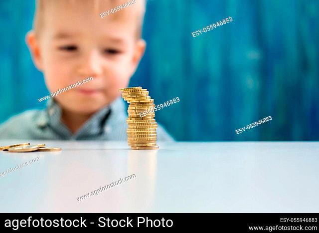 three years old child sitting st the table with money. Happy boy with euro coins. Future childhood and education investment