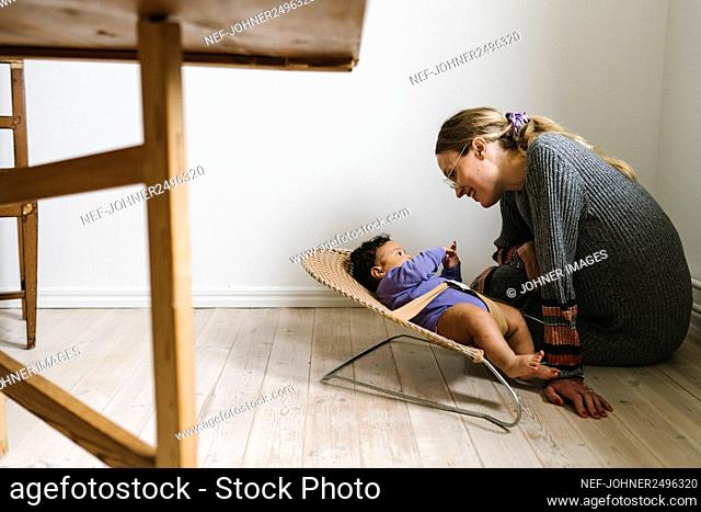 Mother looking at baby lying in bouncer