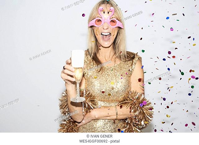 Senior woman wearing golden dress and flmingo shaped glasses, celebtraing New Year's Eve
