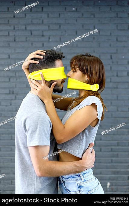Couple with eyes and mouth covered with cloth doing romance by gray wall