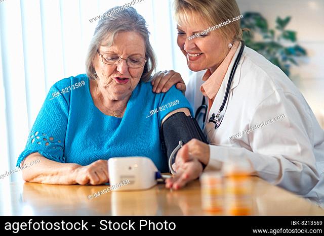 Senior adult woman learning from female doctor to use blood pressure machine
