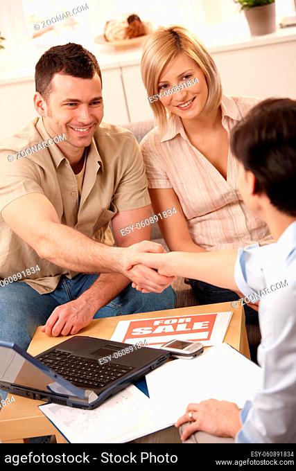 Estate agent shaking hand with young man, making deal with smiling couple in new house