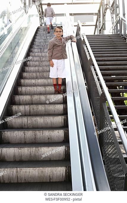 Boy standing on escalator while his brother walking away