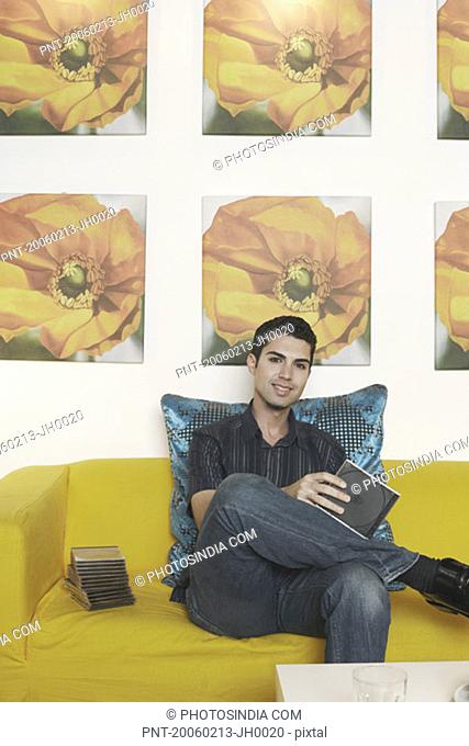 Portrait of a young man sitting on a couch and holding a CD case