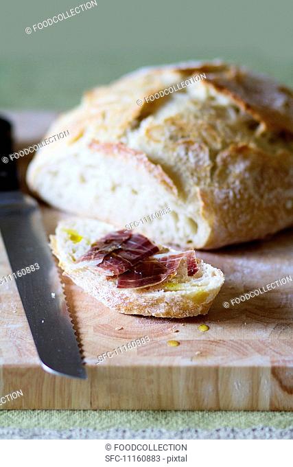 A loaf of bread and a slice of bread topped with cured ham