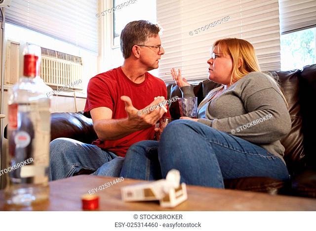 Couple Arguing On Sofa With Bottle Of Vodka And Cigarettes