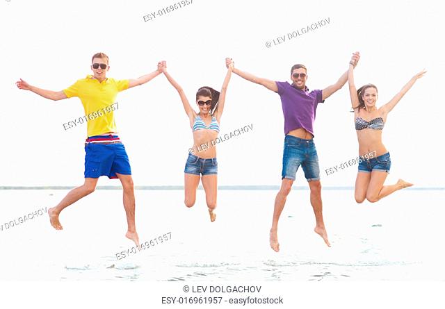 summer holidays, vacation, tourism, travel and people concept - group of happy friends holding hands and jumping on beach