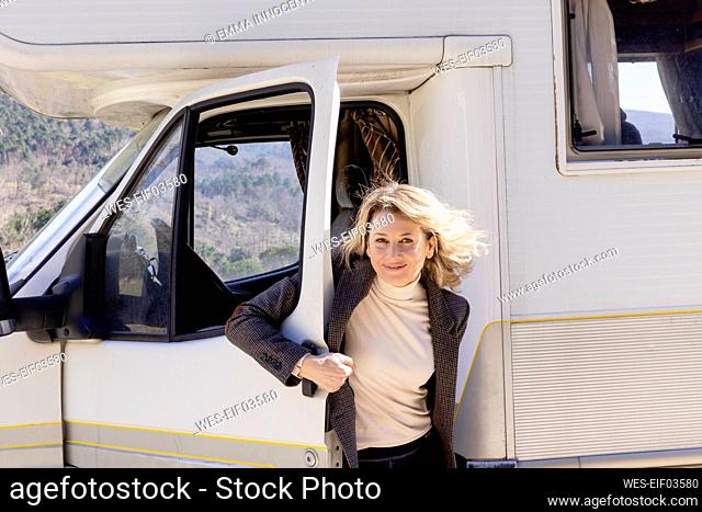 Smiling woman standing by camper trailer door