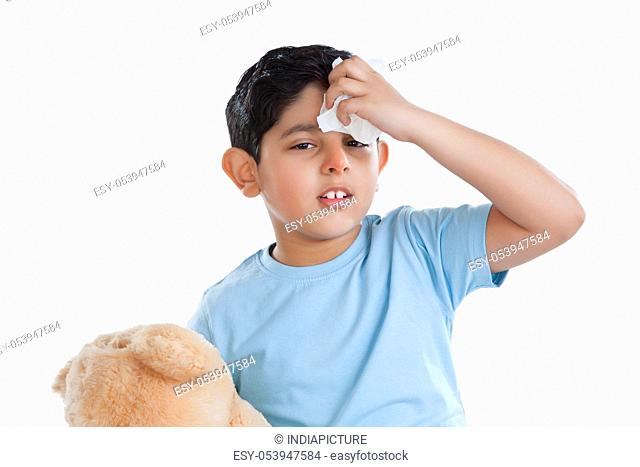 Portrait of little boy putting ice on forehead