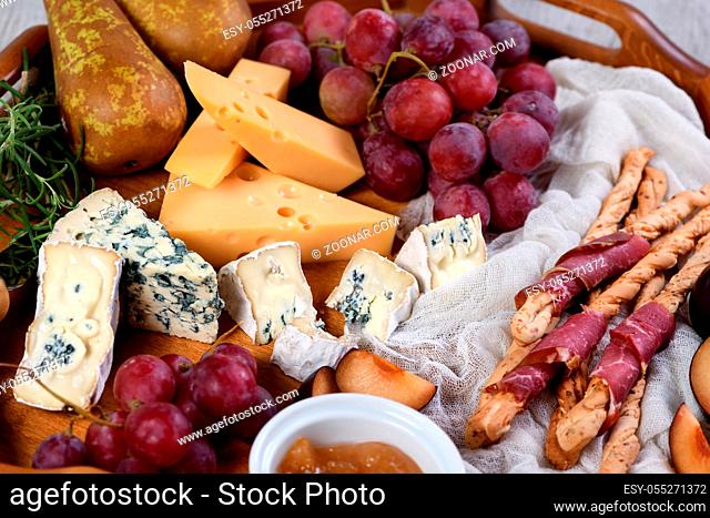 Antipasto. Dish with crispy grissini wrapped in sun-dried bacon, slices of brie cheese, camembert, blue cheese, radamer and muscat grape vine with fruit