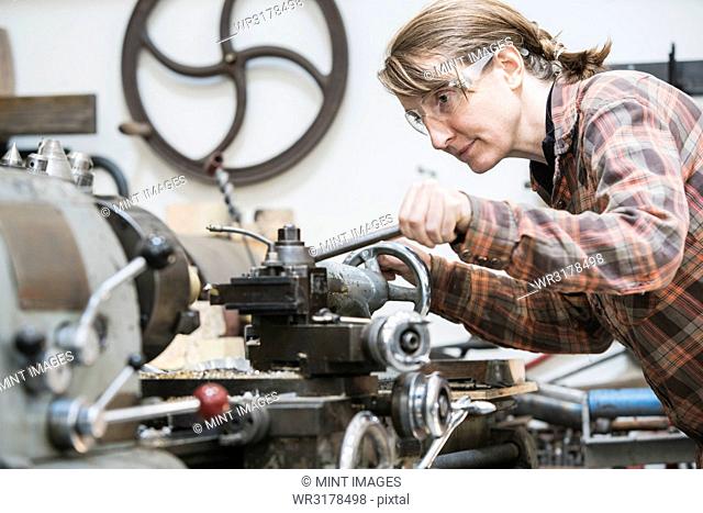 Woman wearing safety glasses standing in a metal workshop, working at metal lathe machine