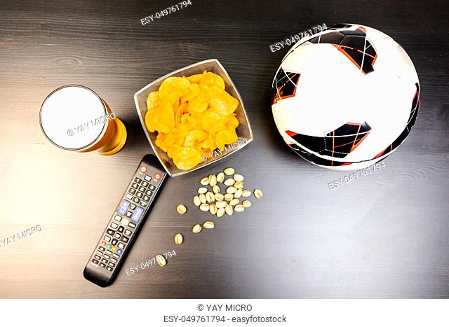 People prepared to watch football on TV with beer. There's beer on the table, ball, TV remote, snacks. Craft beer. Light background