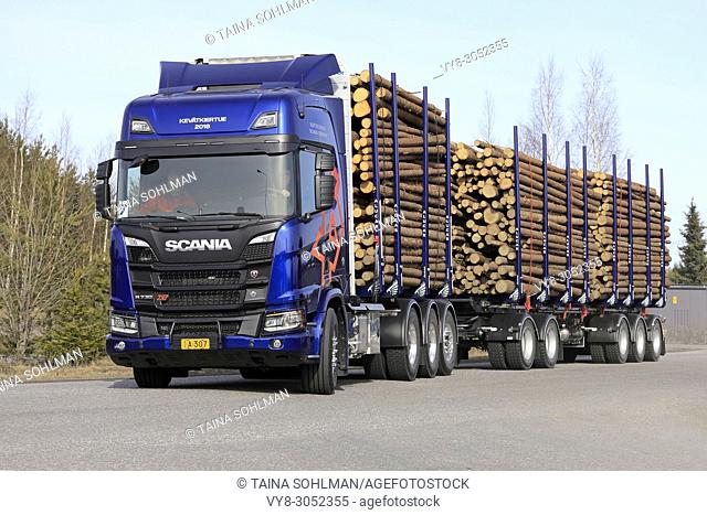 Blue Scania R730 XT logging truck makes left turn on test drive during Scania Tour Turku 2018 in Lieto, Finland - April 12, 2018