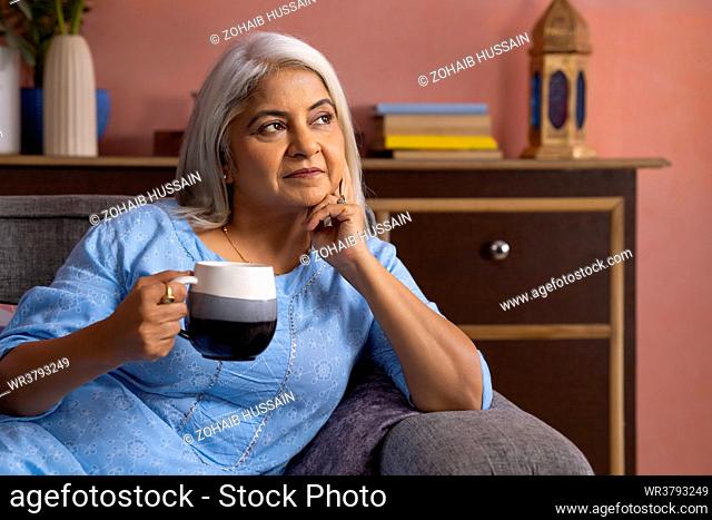 Portrait of a thoughtful old woman looking away with holding a cup of tea in hand