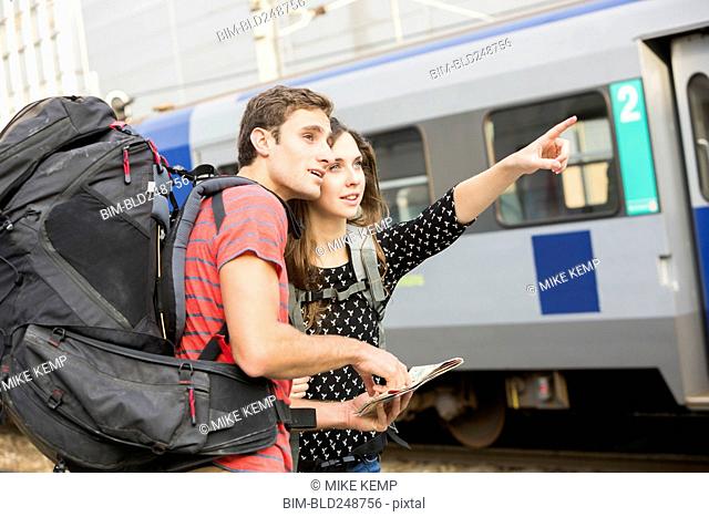 Caucasian couple reading map near train and pointing