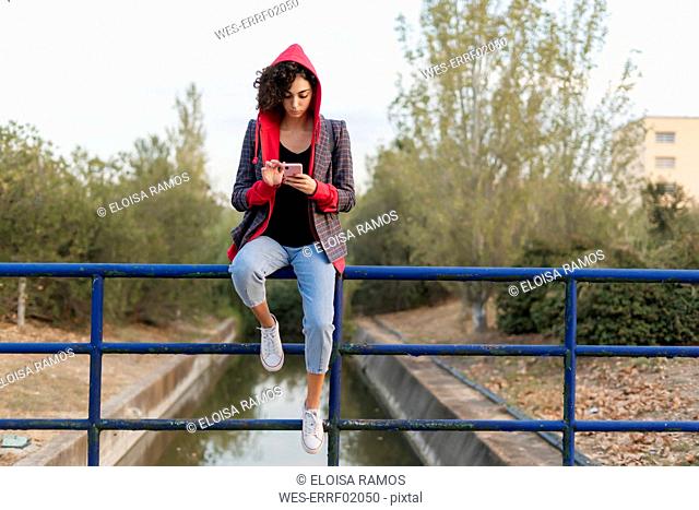 Young woman sitting on railing using mobile phone
