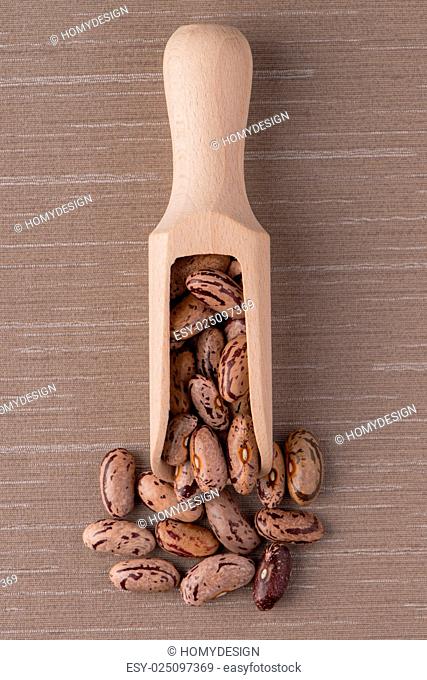 Top view of wooden scoop with pinto beans against brown vinyl background
