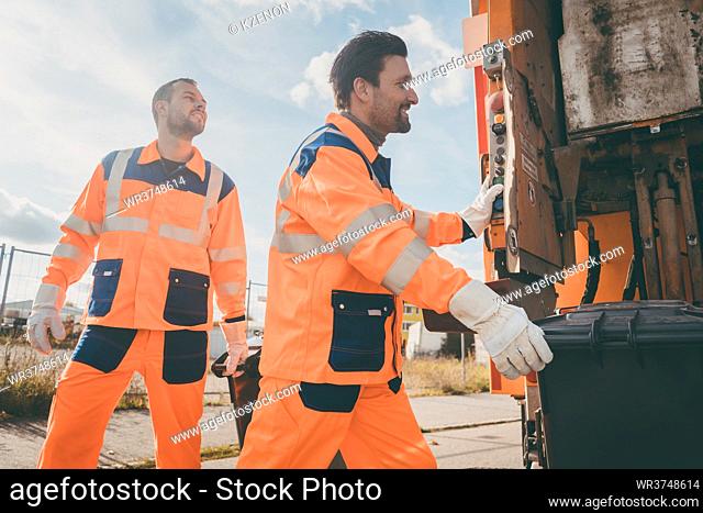 Two garbagemen working together on emptying dustbins for trash removal