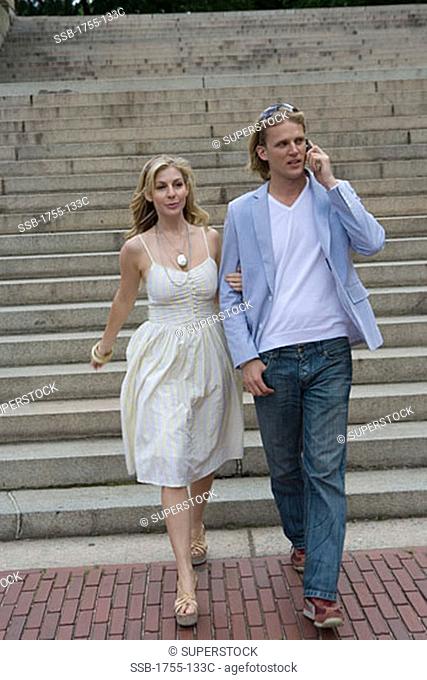Young man talking on a mobile phone and moving down a staircase with a young woman