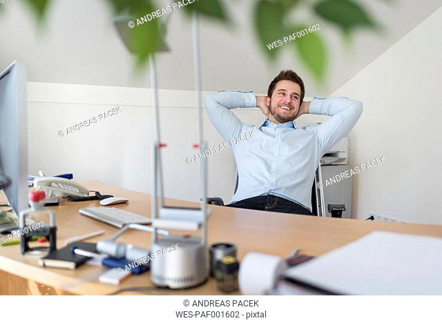 Smiling young man in office leaning back