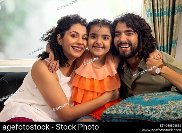 Beautiful girl with her parent posing together while sitting on sofa