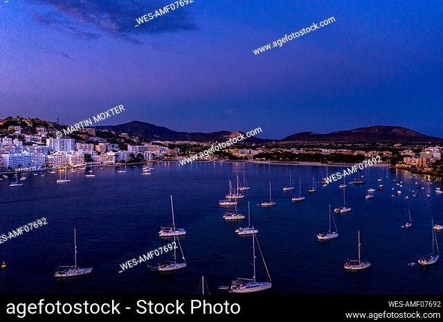 Spain, Mallorca, Santa Ponsa, Boats floating in coastal water at dusk with town in background