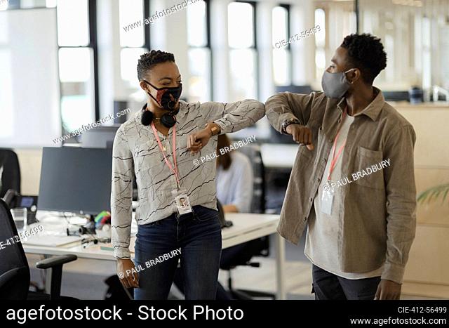 Business people in face masks elbow bumping in office