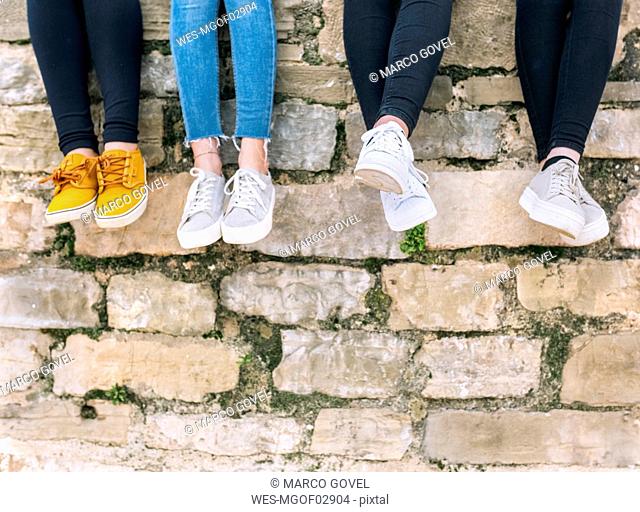 Legs of four friends sitting side by side on a wall
