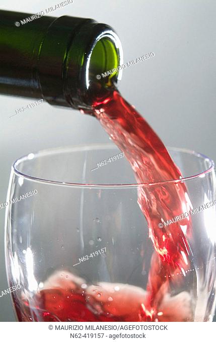 Someone from a green bottle pouring red wine into a wine glass