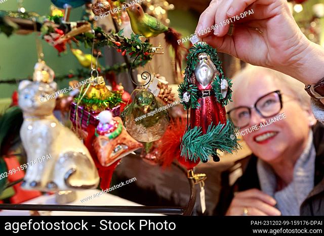 02 December 2023, Saxony-Anhalt, Quedlinburg: Gabriele Velster hangs a Santa Claus figure on her stall. The creator of Advent in den Höfen attracted many...