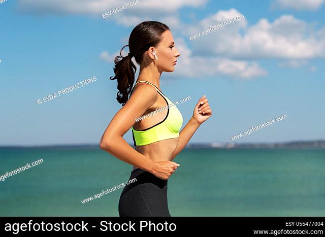woman with wireless earphones running at seaside
