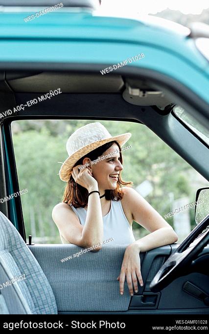 Happy young woman wearing hat leaning on van window