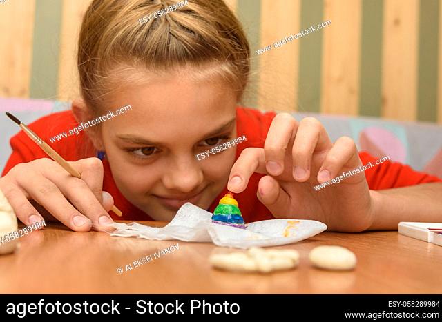 A girl bending over looks at a painted figurine made of salt dough