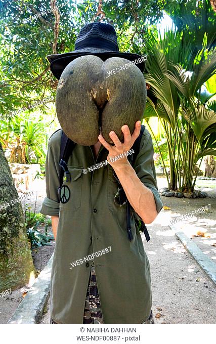 Seychelles, man hiding his face behind huge seed of Coco de Mer
