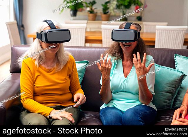 Caucasian senior female friends smiling while using vr headsets in living room at home