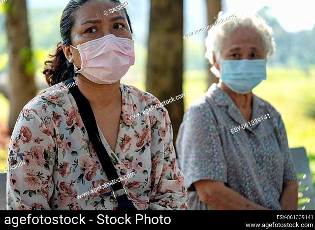 Asian elderly woman and daughter in social distancing sitting bench and wearing face mask for protect safety infection Covid 19 Coronavirus in park