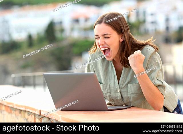 Excited woman watching media on laptop in a coast