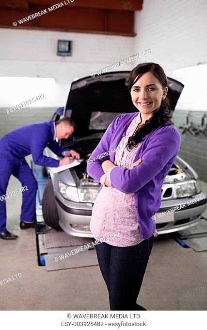 Woman smiling with arms crossed next to a car in a garage