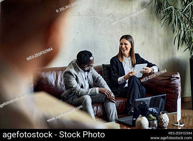 Laughing businessman and businesswoman sitting on couch in hotel lobby