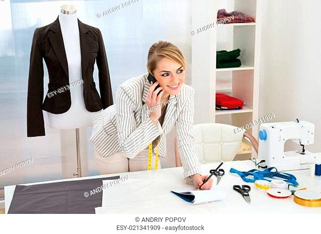 Happy Female Fashion Designer Talking On Cellphone While Writing Note