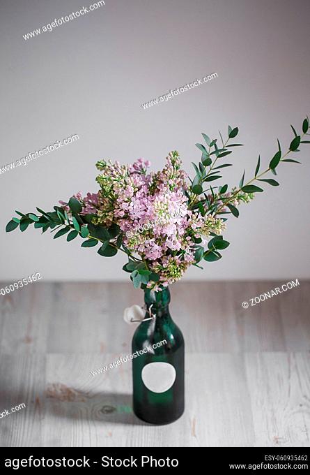 Lilac flower in a green vase on a wooden background