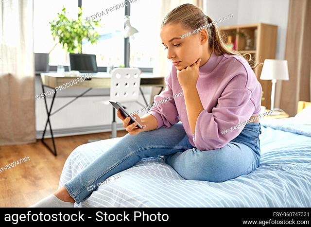 sad girl with smartphone sitting on bed at home